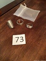 Three sterling silver rings with a small white mesh pouch on wooden surface, ring designs visible.