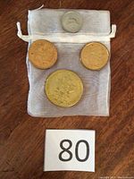 Four coins displayed on a light mesh pouch, including three larger coins and one smaller coin.
