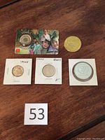 Overview of five coins including three in protective holders, gold-colored coin, and family-themed token