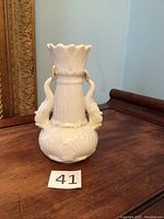 Front view of the cream-colored porcelain dolphin vase showing the fluted rim and dolphin-shaped handles.