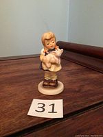 Front view of Goebel Hummel figurine showing girl holding pig on wooden surface with item number 31 displayed.