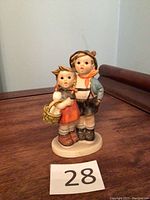 Full view of the Hummel 'Surprise' figurine showing boy and girl children in traditional attire on wooden surface.