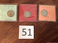 Three sealed coins dated 1947, 1948, and 1949 with colored backing (green, red, orange) and handwritten year labels.