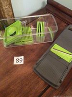 Slicer base unit with multiple green blade inserts in a clear plastic container on a wooden table.
