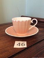 Pink Susie Cooper cup and saucer shown on wooden surface, cup placed inside the saucer showing scalloped white trim and vertical fluted pattern on both pieces.