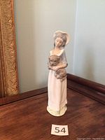 Full view of the Tenora figurine showing the woman standing and holding a dog, placed on a wooden surface with a plain background.
