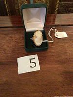 Ring in green hinged jewelry box on wood table next to lot number card '5'.