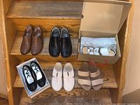 All six pairs of shoes arranged on wooden steps showing different styles and colors including brown, black, white, and tan.