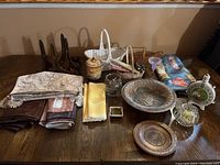 Overview of the assorted lot showing table linens, baskets, pottery bowl, wooden plate, candles, glass decorative items, and small scale.