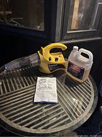 Full view of the bug fogger machine with jug of liquid and instruction manual on metal table.