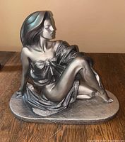 Front angle view of the silver-painted Art Deco statue of a seated woman titled 'Cameo' showing draped clothing and flowing hair.