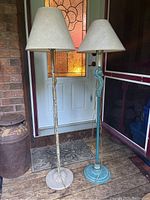Two floor lamps placed side by side showing height and base details, with the beige shades on both, gold tone one taller missing finial hold on shade.