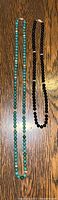 Two necklaces laid flat: one turquoise-green jade bead necklace approximately 33 inches long and one black onyx bead necklace approximately 22 inches long.