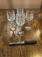 Four vintage crystal glasses with etched pineapple designs, arranged on a wooden surface next to a marker for size reference.
