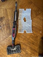 Full view of Shark Genius steam mop and a reusable cleaning pad laid out on floor.