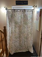 Full view of floral patterned shower curtain hanging on adjustable metallic tension rod in bathroom setting with wall sconces and stair railing.