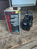 Red Lion Submersible Utility Pump next to its original box on wooden flooring.