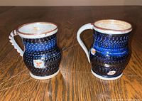 Front and side view of two blue pottery mugs with textured exterior, painted small detail, and brown rim.