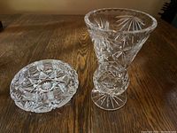 Crystal vase next to round ash tray on wooden table, showing overall shape and design.