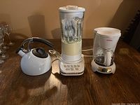 Wide view showing all three appliances on a wooden table: the KitchenAid blender, OXO kettle, and Sunbeam coffee maker.