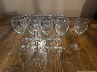 Photo showing a set of 9 clear wine glasses arranged in two rows on a wooden surface, with 8 standard sized glasses and 1 smaller glass distinct on the right side.