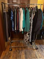 Full rack of assorted women's medium/large clothing items including pants, tops, dresses, and outerwear on a rolling garment rack