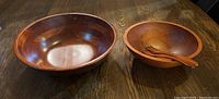 Photo showing two wooden bowls on a wooden table surface, large bowl on left and smaller bowl on right with wooden salad fork and spoon inside.