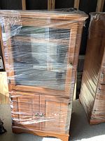 Front view of wooden cabinet wrapped in plastic showing glass door and lower doors