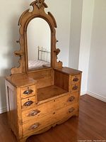 Front view of antique wooden dresser with large ornate arched mirror and multiple drawers.