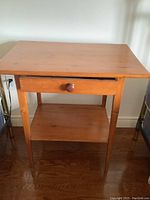 Front view of antique pine endtable showing single drawer and lower shelf, sitting on hardwood floor.