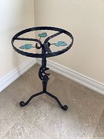 Full view of the black artisan metal side table showing twisted metal legs and circular top with green leaf designs.
