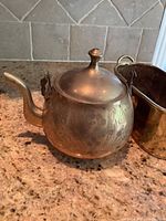 Small brass teapot showing floral engraving and curved spout, with lid finial