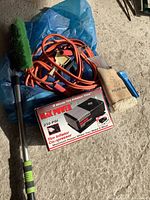 Photo showing all items in lot with tire inflator box, jumper cables, gloves, and car brush laid on concrete floor