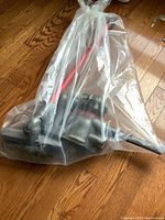 Complete cordless vacuum assembly in clear plastic bag showing red wand, motor unit and floor head