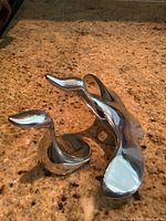 Photo of two polished metal bird figurines on a speckled granite countertop showing their reflective, smooth surfaces and modern abstract shapes.