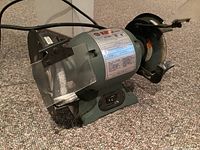Photo showing the full side view of KING Canada bench grinder with grinding wheel and wire brush wheel installed, protective transparent guard fitted on the grinding wheel.