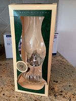 Full view of the Lamplight Farms hurricane lamp in original box showing the clear ribbed glass base and glass chimney.