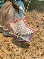 Close-up photo focusing on the delicate lace-trimmed umbrella with pink and white ruffles held by the figurine.