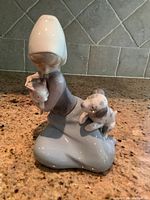 Front angle view of Lladro porcelain figurine showing girl holding a dog and another dog by her side, on granite surface with tile background.