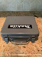 Closed gray plastic carrying case with Makita label on top, resting on granite countertop.