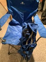 Single blue Outbound outdoor folding lawn chair with padded armrests, folded second chair beside it.