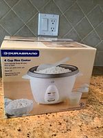 Photo showing the original box for Durabrand 4 cup rice cooker with product image and features