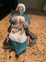 Front angle showing woman seated, sewing, with teddy bear on lap and basket on floor