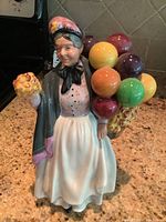 Front view of the Royal Doulton figurine showing the woman holding a basket with colorful balloons and yellow flowers.