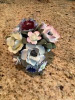 Top down view of multi-flower porcelain bouquet with cream, blue, pink, purple flowers and green leaves.