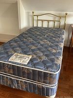 Full side view of mattress and box spring with brass headboard in background.