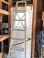 Full view of aluminum step ladder with five wide steps and cross bracing, standing upright.