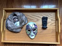 View of entire hardwood tray containing two ceramic masks and one small carved figurine