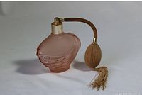 Pink frosted glass vintage perfume bottle shaped like a seashell with brass-tone top and attached fabric atomizer bulb with tassel.