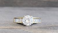 Close-up of gold tone ring front view showing round central clear stone and baguette stones on band